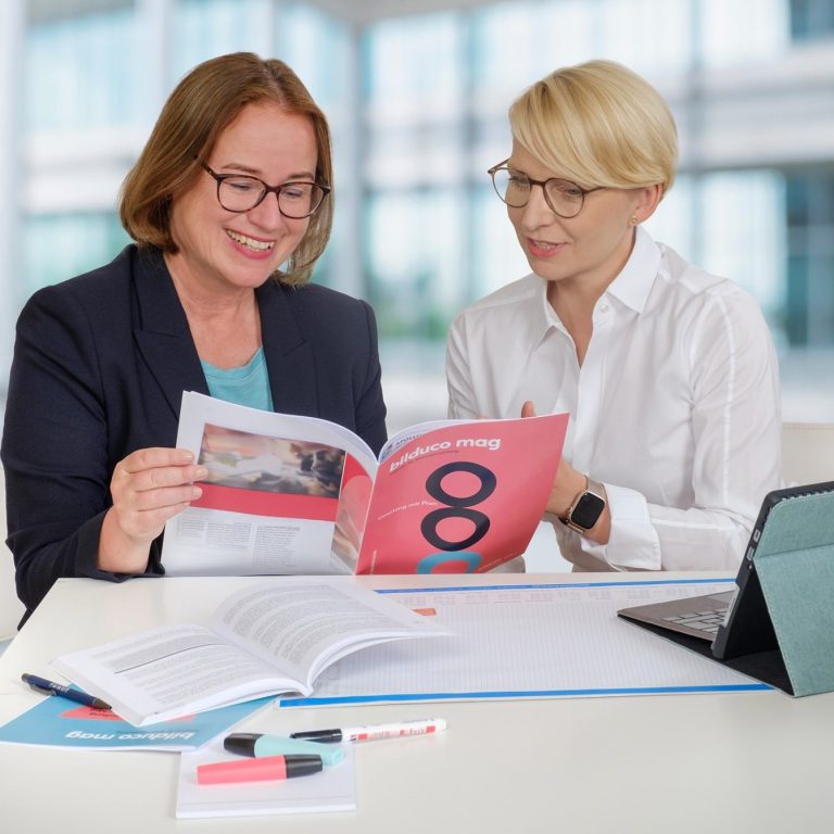 Zwei Frauen lesen und diskutieren gemeinsam in einem modernen Büro.