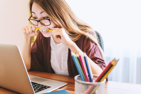 Frau mit Brille sitzt am Schreibtisch und schaut nervös auf einen Laptop.