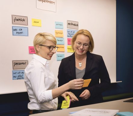 Zwei Frauen betrachten gemeinsam bunte Notizen an einer Wand.